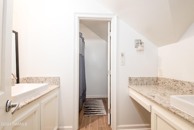 full bath featuring vaulted ceiling, wood finish floors, vanity, and baseboards