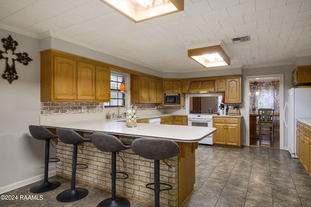 kitchen featuring white appliances, ornamental molding, kitchen peninsula, and a kitchen breakfast bar