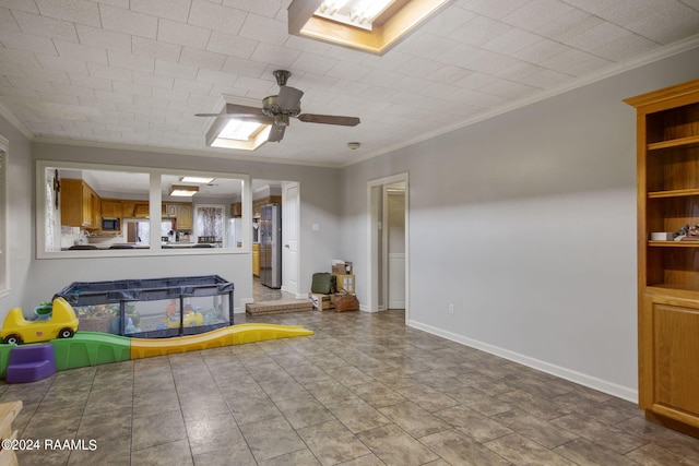 unfurnished living room featuring ceiling fan, ornamental molding, and a skylight