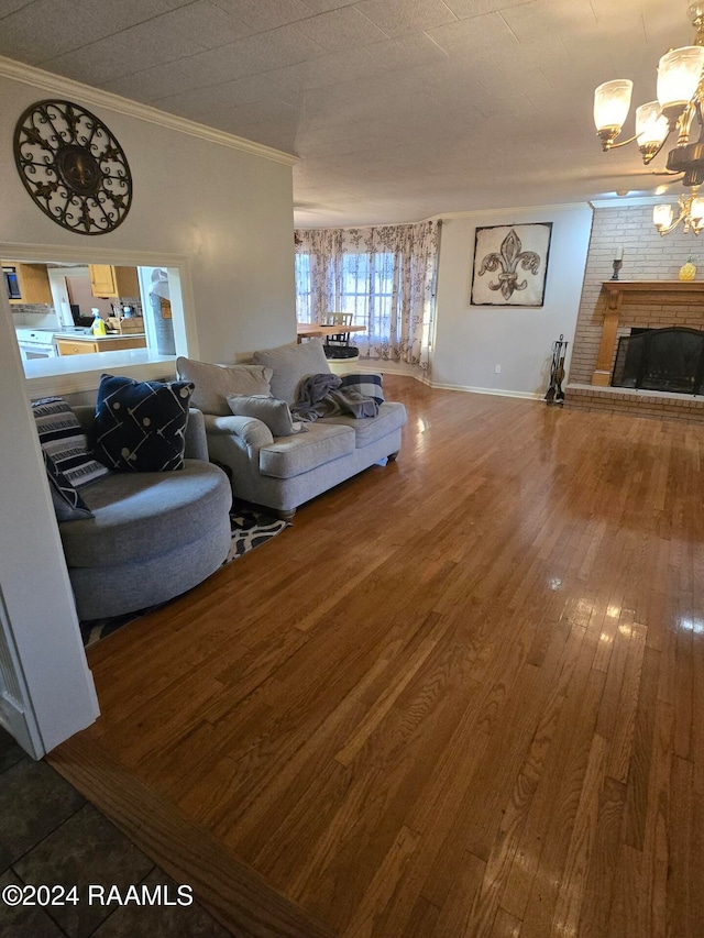 living room with an inviting chandelier, wood-type flooring, crown molding, and a brick fireplace