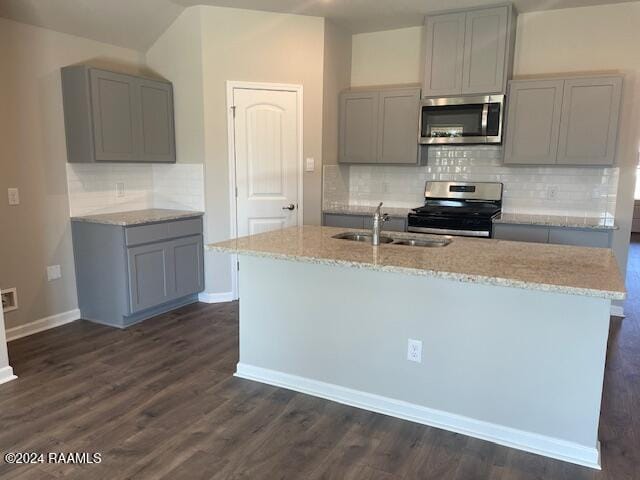 kitchen featuring light stone counters, a center island with sink, a sink, gray cabinetry, and stainless steel appliances