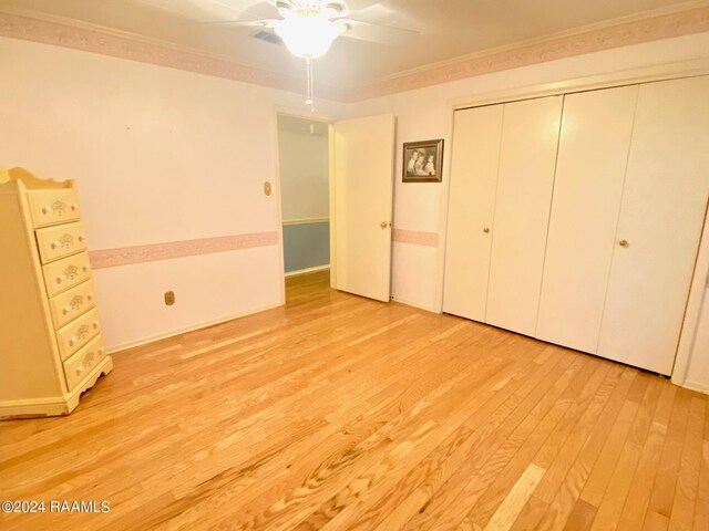 unfurnished bedroom featuring light hardwood / wood-style floors, ornamental molding, ceiling fan, and a closet