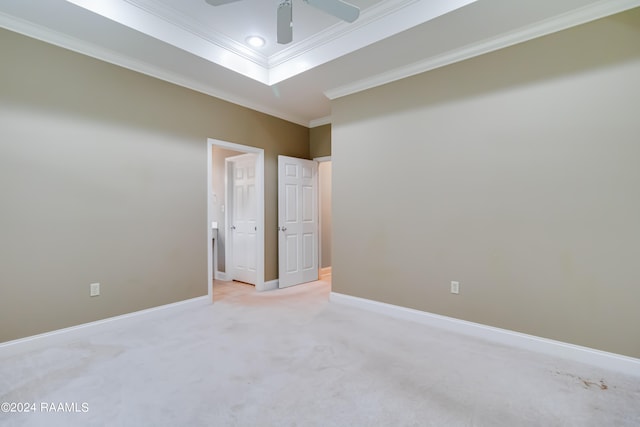 empty room with ceiling fan, a tray ceiling, crown molding, and light carpet