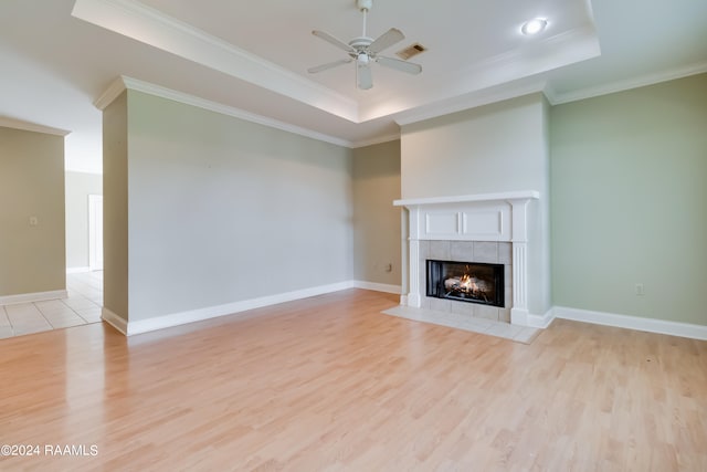 unfurnished living room featuring ceiling fan, light wood-type flooring, a tray ceiling, and a tile fireplace