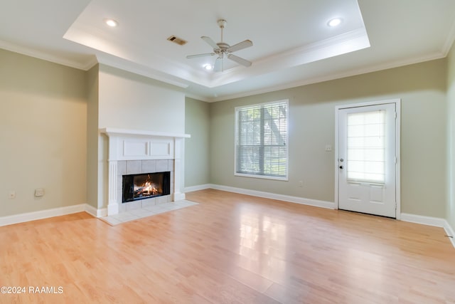 unfurnished living room featuring light hardwood / wood-style floors, a fireplace, a tray ceiling, and ceiling fan