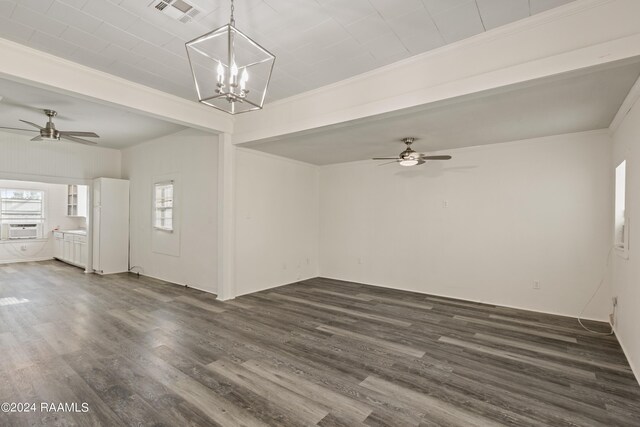 empty room with visible vents, ornamental molding, ceiling fan with notable chandelier, dark wood-style floors, and cooling unit