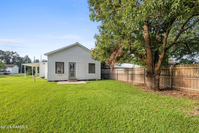 rear view of property featuring entry steps, a carport, a yard, and fence