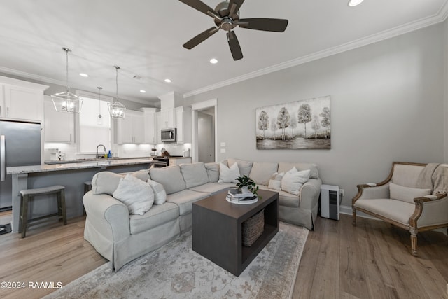 living room with ornamental molding, sink, ceiling fan with notable chandelier, and light hardwood / wood-style floors