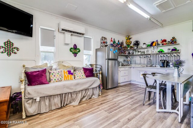 bedroom featuring a wall mounted AC, light hardwood / wood-style floors, stainless steel refrigerator, and sink