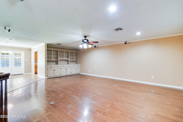 unfurnished living room featuring a textured ceiling, visible vents, baseboards, light wood finished floors, and crown molding