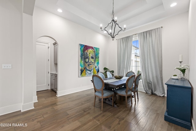 dining area featuring a notable chandelier, a raised ceiling, and dark hardwood / wood-style flooring