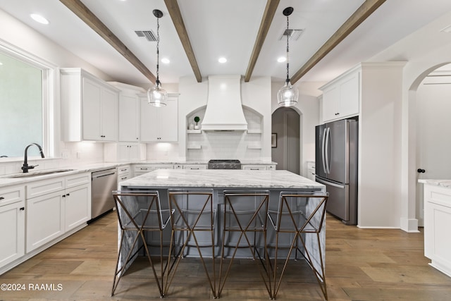 kitchen with appliances with stainless steel finishes, a kitchen island, hardwood / wood-style floors, premium range hood, and sink