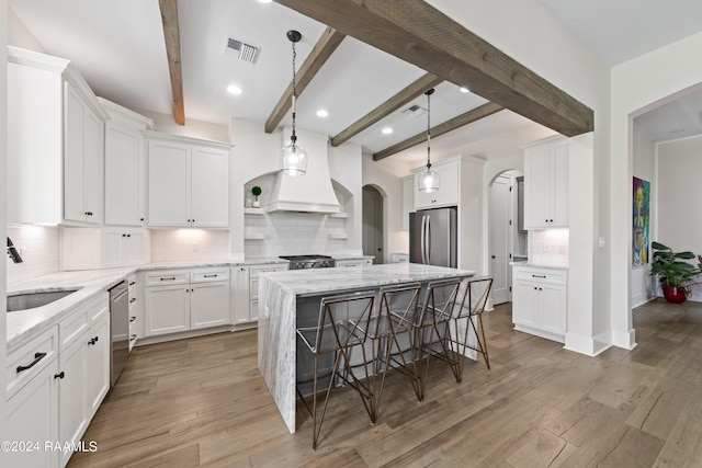 kitchen featuring beamed ceiling, wood-type flooring, backsplash, appliances with stainless steel finishes, and a center island