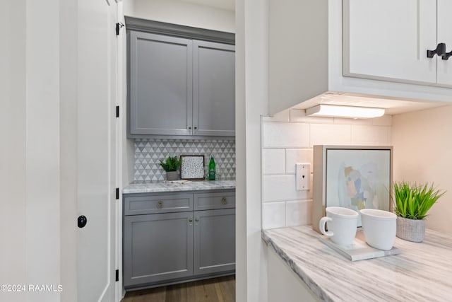 bar featuring gray cabinets, decorative backsplash, light stone counters, and dark hardwood / wood-style flooring