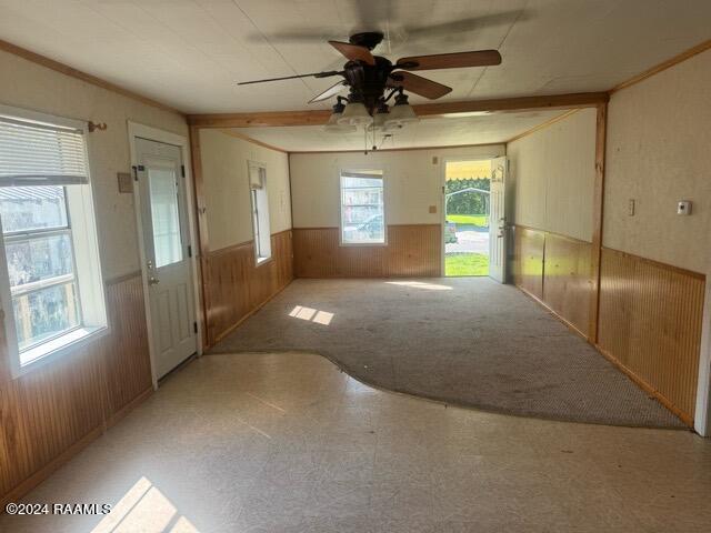 carpeted spare room with ceiling fan, wooden walls, and crown molding