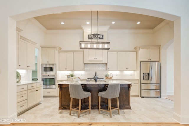 kitchen with an island with sink, appliances with stainless steel finishes, a kitchen breakfast bar, light stone countertops, and pendant lighting