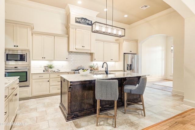 kitchen featuring appliances with stainless steel finishes, light hardwood / wood-style flooring, decorative light fixtures, and a center island with sink