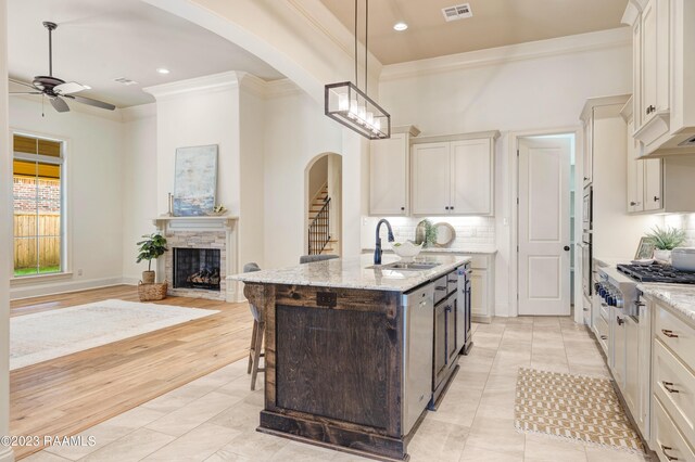 kitchen featuring light stone countertops, hanging light fixtures, stainless steel appliances, ornamental molding, and a center island with sink