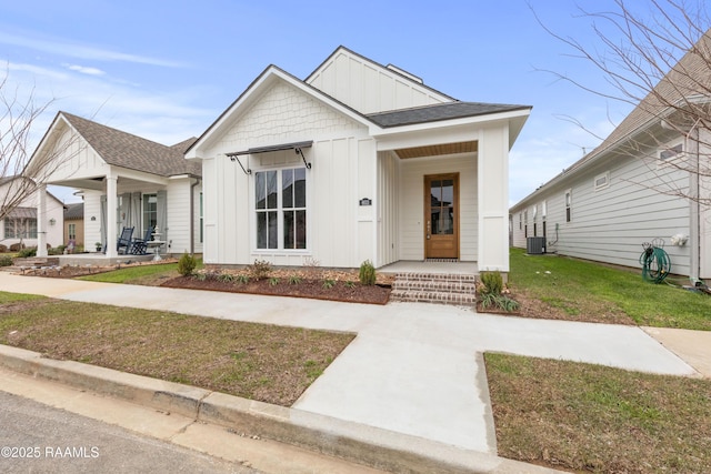 modern inspired farmhouse with board and batten siding, roof with shingles, a porch, central AC, and a front yard