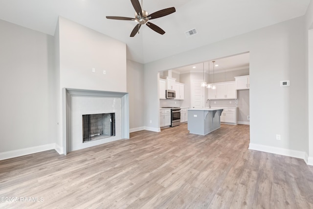 unfurnished living room with a fireplace, a sink, visible vents, baseboards, and light wood finished floors