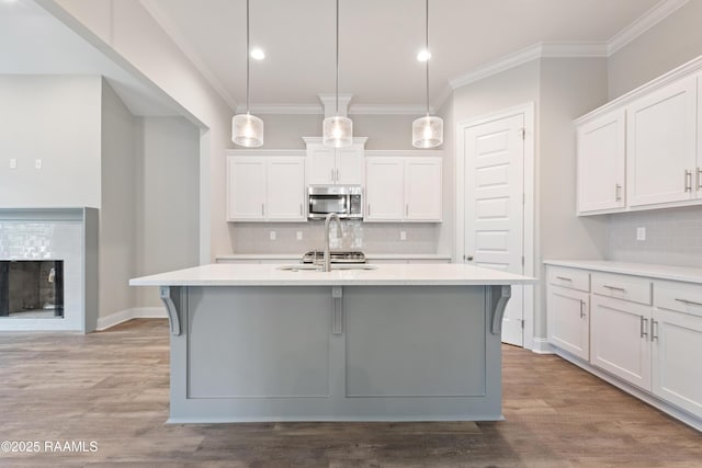 kitchen featuring hanging light fixtures, stainless steel microwave, light countertops, and white cabinets