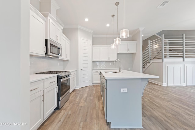 kitchen featuring appliances with stainless steel finishes, a kitchen island with sink, light countertops, and white cabinetry