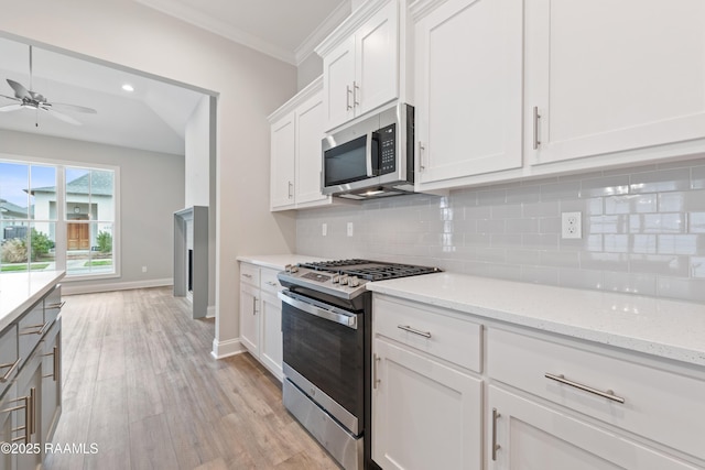 kitchen featuring tasteful backsplash, appliances with stainless steel finishes, white cabinetry, light stone countertops, and light wood-type flooring