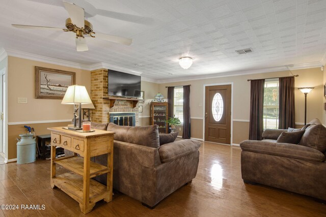 living room featuring crown molding, hardwood / wood-style flooring, a brick fireplace, and ceiling fan