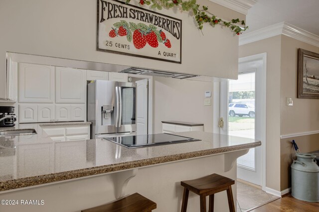 kitchen featuring a breakfast bar, light stone counters, stainless steel fridge, and white cabinetry