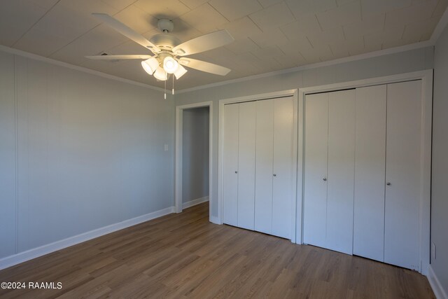 unfurnished bedroom featuring ceiling fan, multiple closets, crown molding, and hardwood / wood-style floors