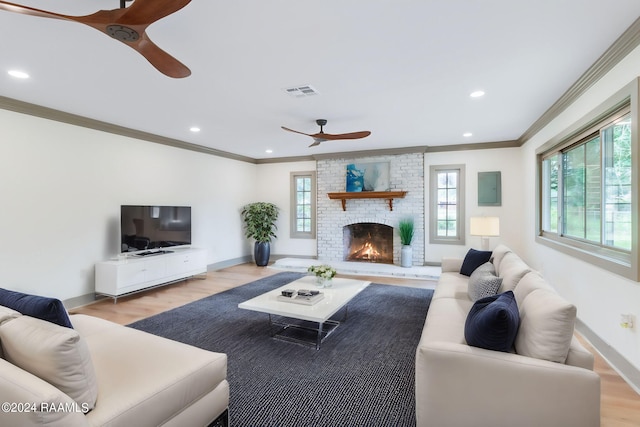 living room with light hardwood / wood-style flooring, a brick fireplace, ceiling fan, and crown molding