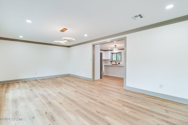 unfurnished room featuring ornamental molding, an inviting chandelier, and light hardwood / wood-style flooring