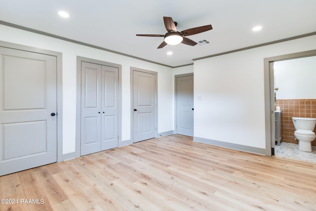 unfurnished bedroom featuring ceiling fan, connected bathroom, tile walls, multiple closets, and light wood-type flooring