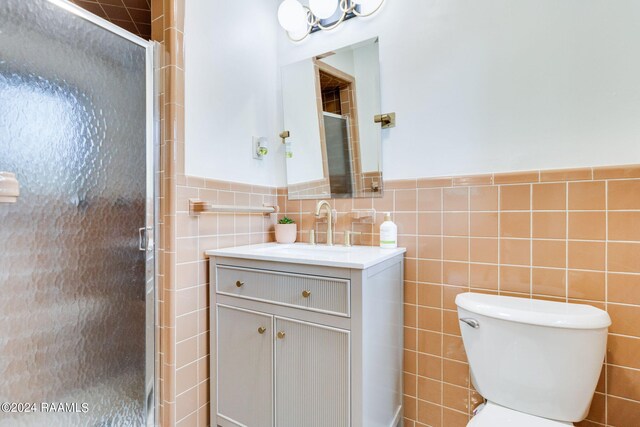 bathroom with vanity, tile walls, toilet, and a shower with door