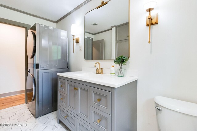 bathroom featuring stacked washing maching and dryer, tile patterned floors, crown molding, vanity, and toilet