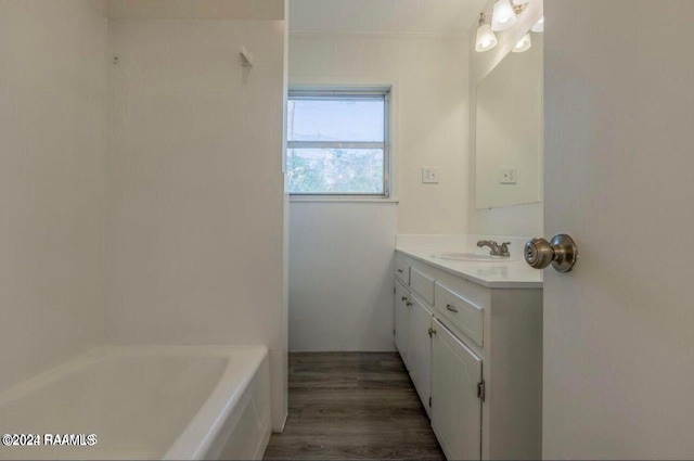 bathroom with wood-type flooring, a washtub, ornamental molding, and vanity