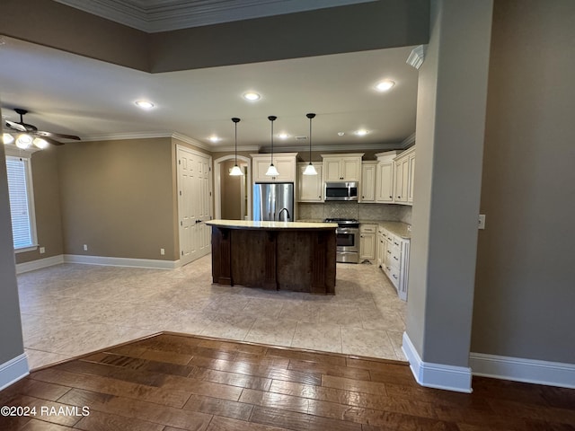 kitchen featuring crown molding, stainless steel appliances, ceiling fan, pendant lighting, and a center island with sink