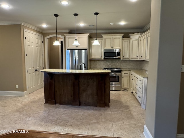 kitchen featuring decorative light fixtures, appliances with stainless steel finishes, a kitchen island with sink, ornamental molding, and cream cabinetry