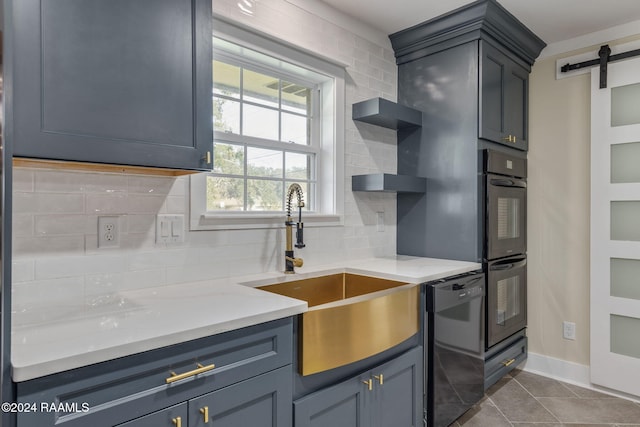 kitchen featuring decorative backsplash, dark tile patterned floors, sink, black appliances, and a barn door