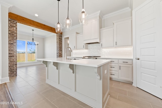 kitchen with a sink, light countertops, backsplash, an island with sink, and crown molding