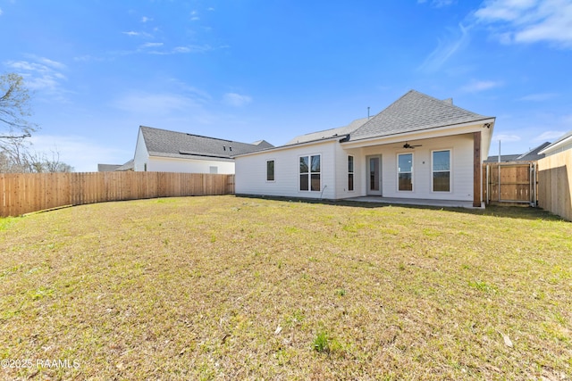 back of house with a ceiling fan, a fenced backyard, a lawn, and roof with shingles