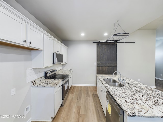 kitchen featuring white cabinetry, sink, appliances with stainless steel finishes, light hardwood / wood-style flooring, and a barn door