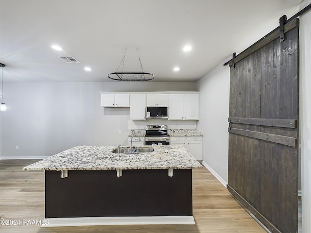 kitchen with a kitchen island with sink, white cabinetry, a barn door, and stainless steel appliances