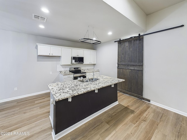 kitchen featuring stainless steel appliances, a center island with sink, a barn door, white cabinetry, and light wood-type flooring