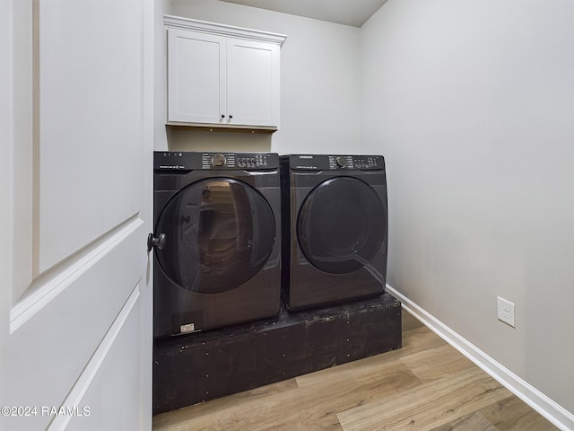 laundry room featuring light wood-type flooring, washing machine and dryer, and cabinets