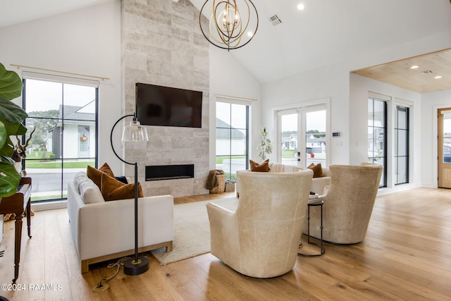 living room featuring a tiled fireplace, high vaulted ceiling, a chandelier, and light hardwood / wood-style floors