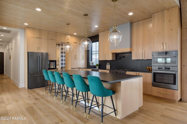 kitchen featuring appliances with stainless steel finishes, light brown cabinetry, decorative light fixtures, and light hardwood / wood-style floors