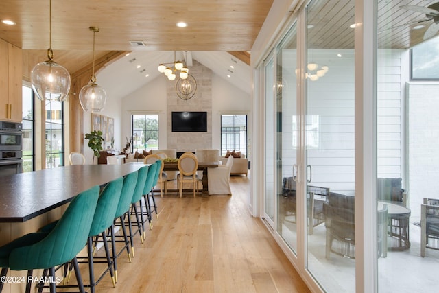 dining space with an inviting chandelier, wooden ceiling, light hardwood / wood-style flooring, beam ceiling, and a large fireplace