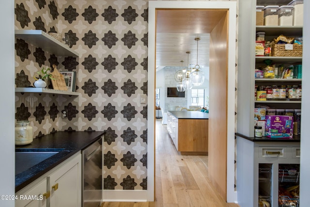 interior space with white cabinets, dark stone countertops, light wood-type flooring, sink, and pendant lighting