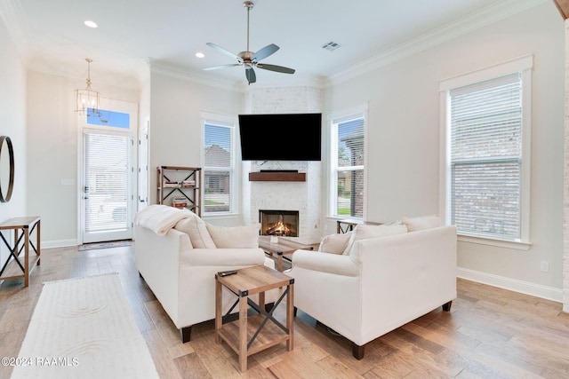 living room featuring crown molding, ceiling fan with notable chandelier, light wood-type flooring, and a fireplace